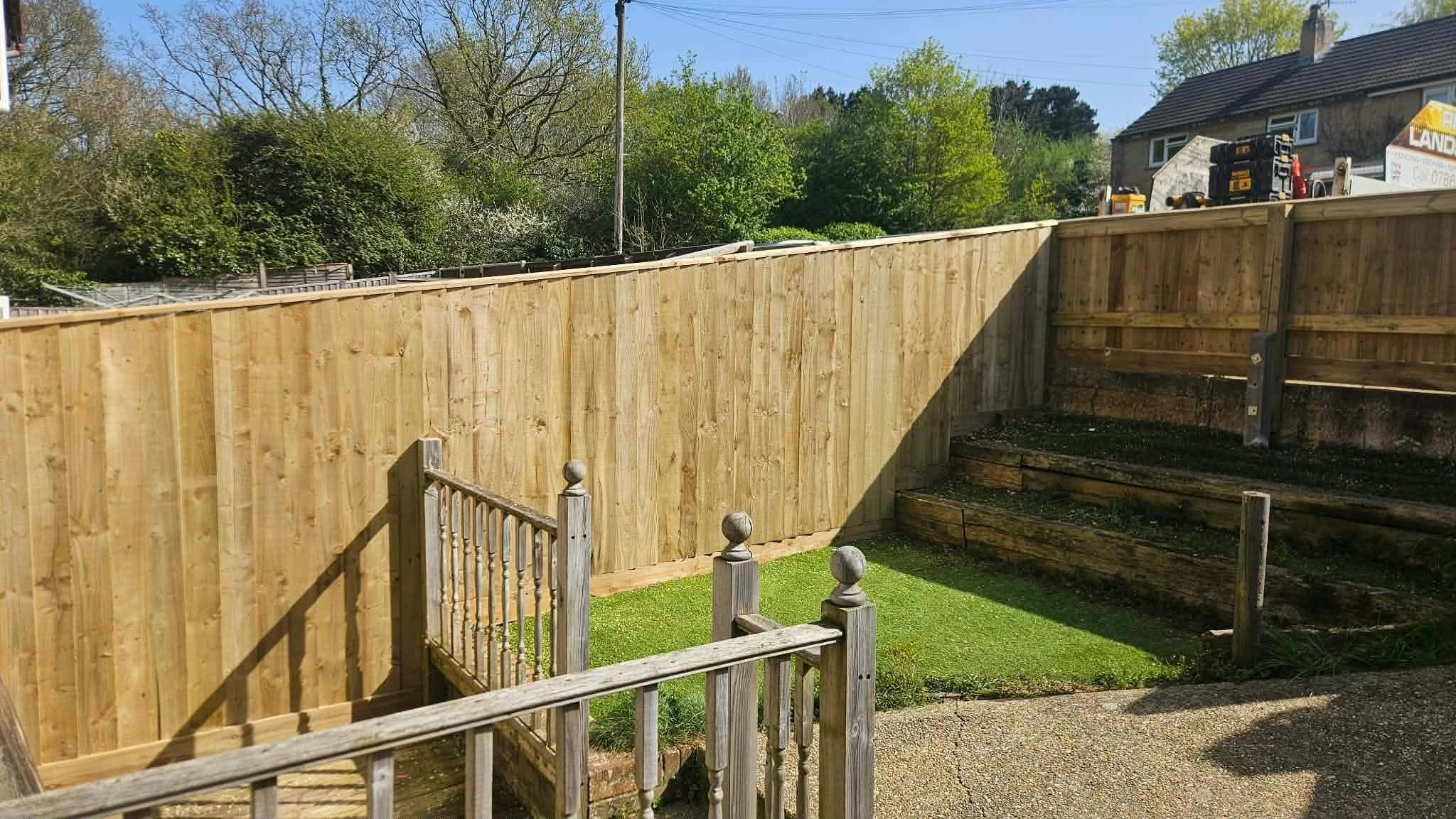 A new close-board fence around a lawn, with timber sleeper steps and railings